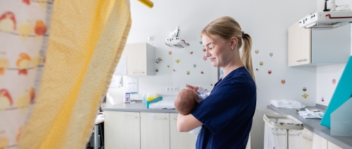 Kinderkrankenschwester im Untersuchungszimmer der Wochenbettstation mit Baby im Arm