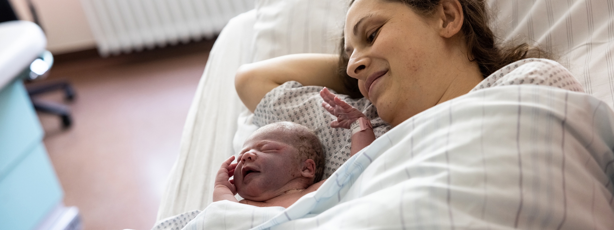 Mama im Patientenbett mit Neugeborenen unter dem Arm