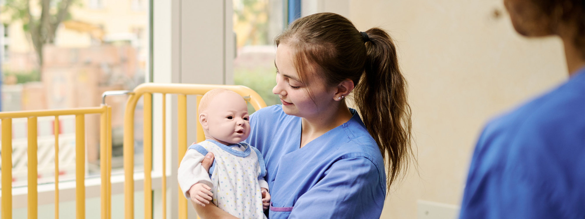 Hebammenstudentin mit Babypuppe am Gitterbett