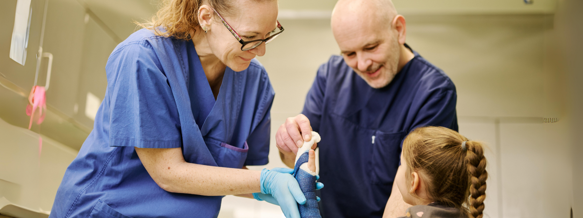 Arzt und Assistentin legen Gips um den Arm der kleinen Patientin